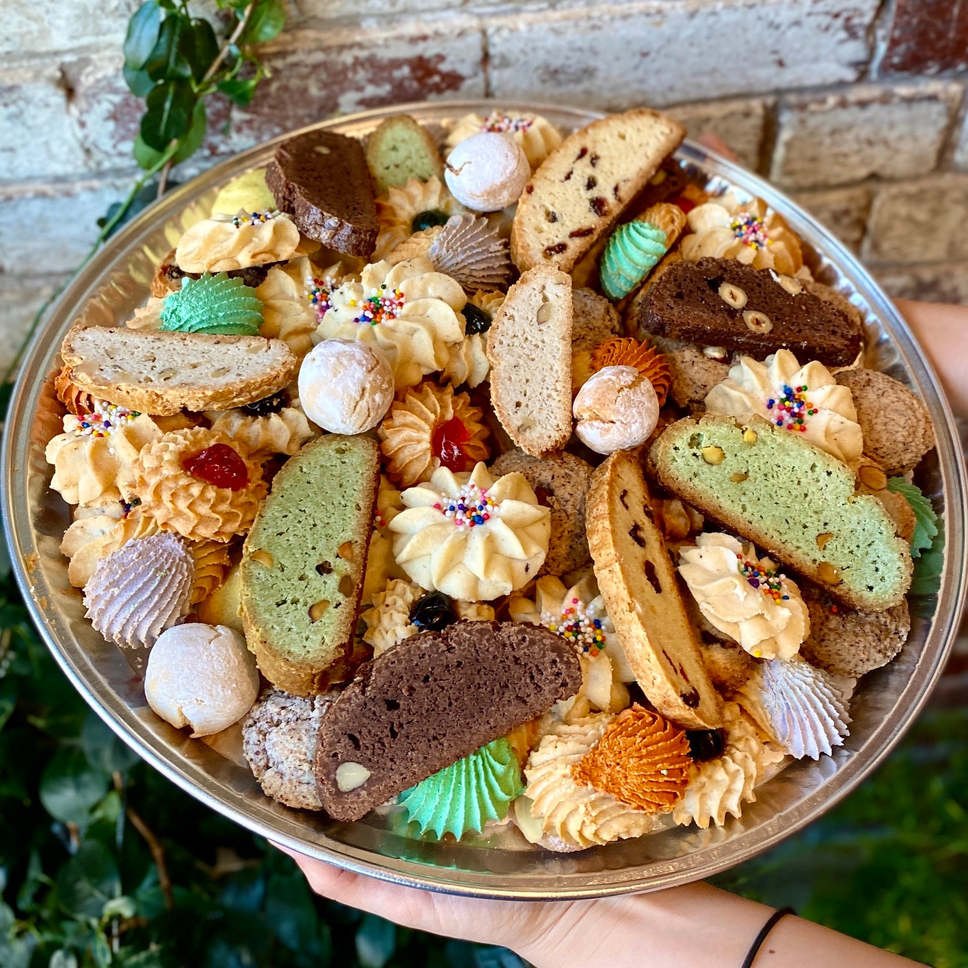 A person holding a tray of assorted cookies in a bakery