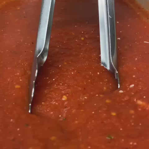 Pizza skull being lifted from tomato sauce with tongs