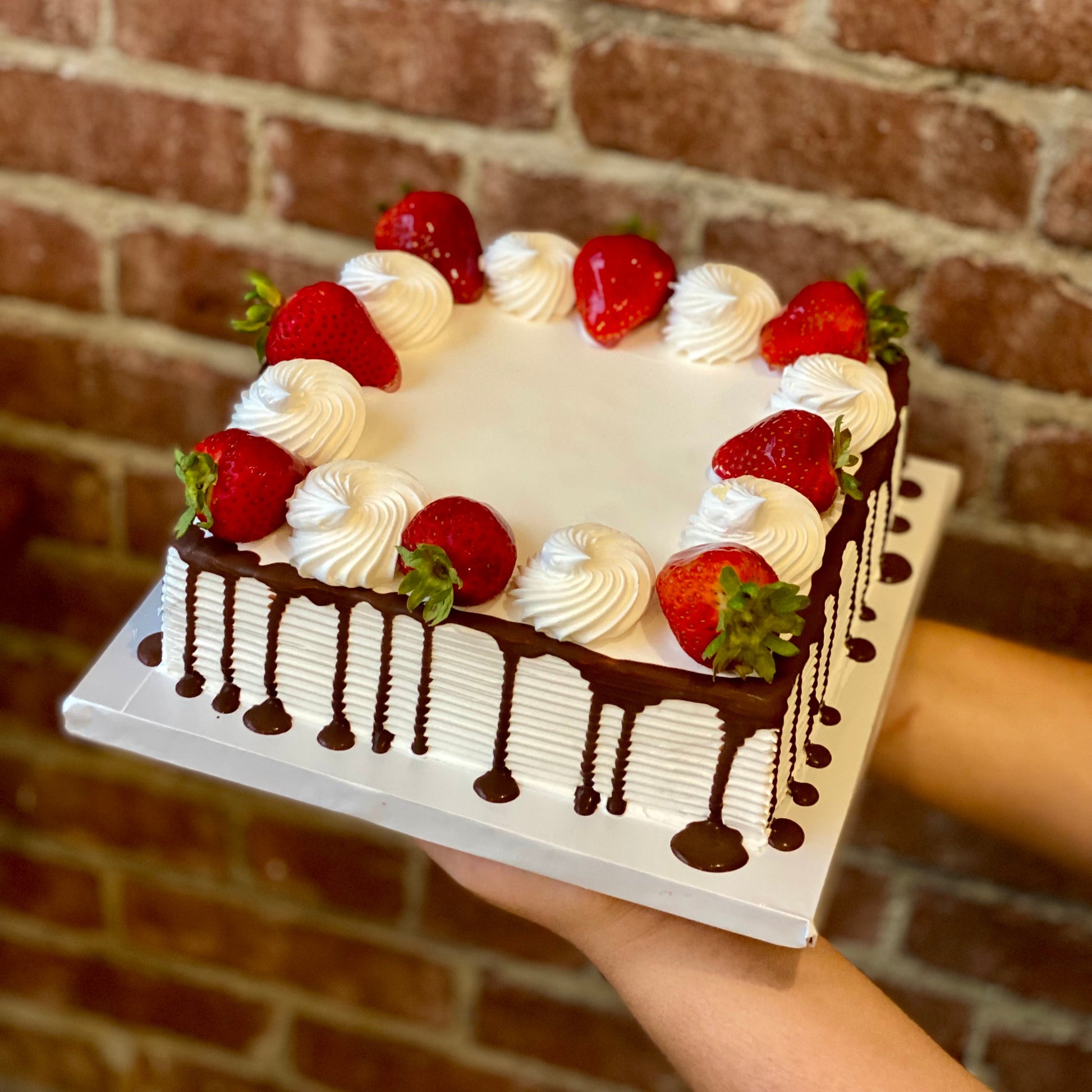 Square white cake with chocolate drip and fresh strawberries