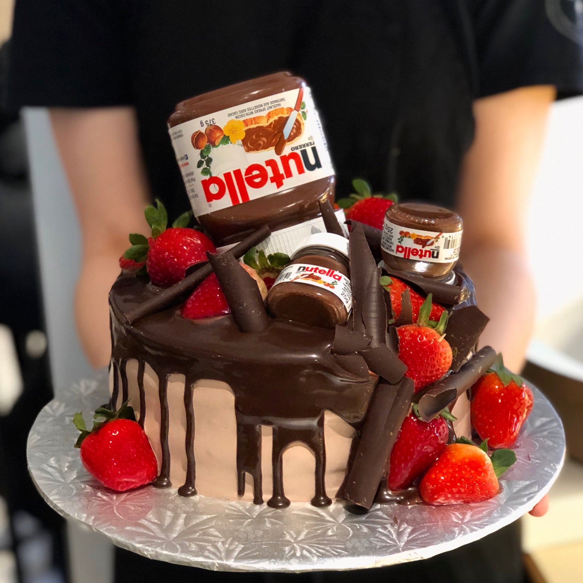 Chocolate cake with Nutella jars on top and fresh strawberries